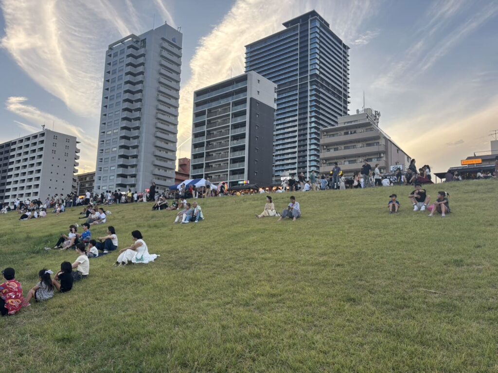 17時30分ごろの淀川河川敷で、ミナモランタンを待つ多くの来場者が堤防や芝生に集まる様子
