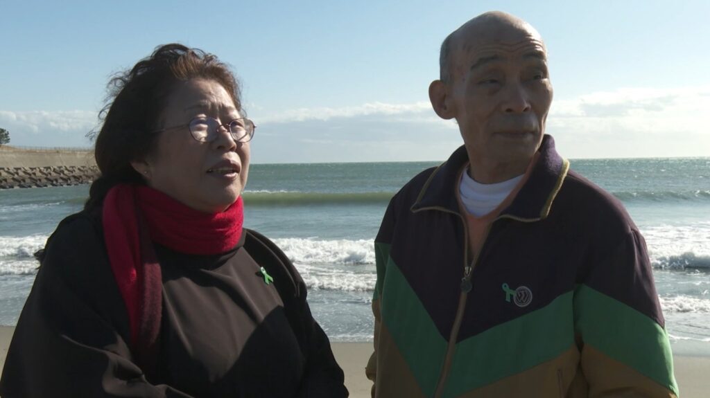 海辺で並んで歩く石川一雄さんと早智子さん。映画『うそがほんとに ほんとがうそに』の場面写真
